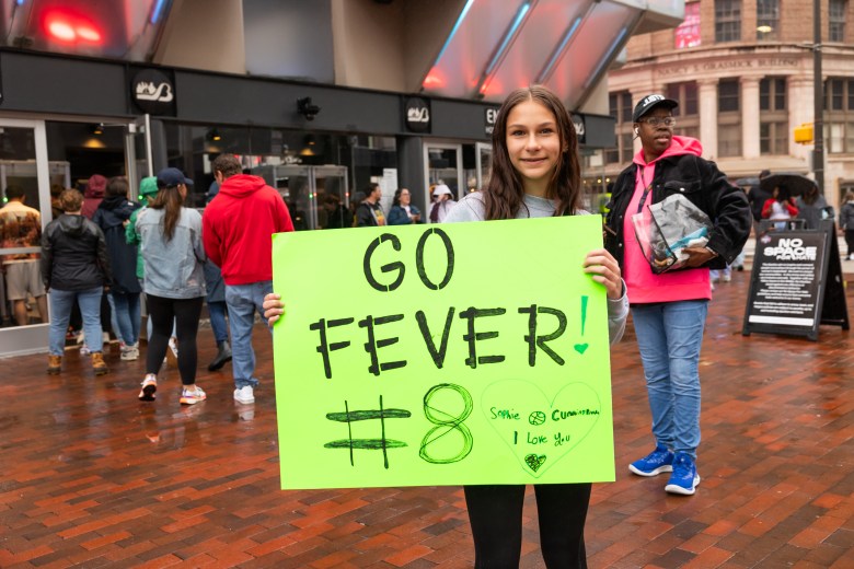 A smiling young person holds a sign that says "Go Fever! #8"