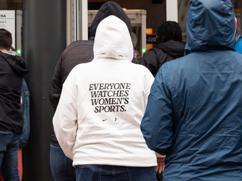 A person wearing a white hoodie that says "everyone watches women's sports."