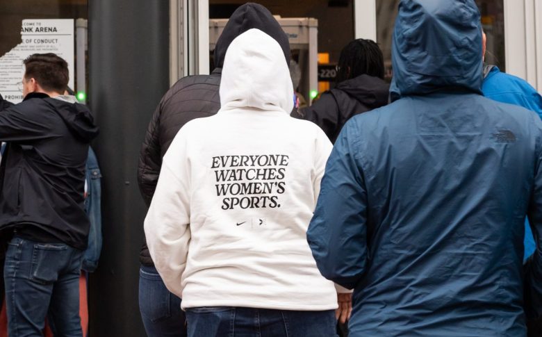 A person wearing a white hoodie that says "everyone watches women's sports."