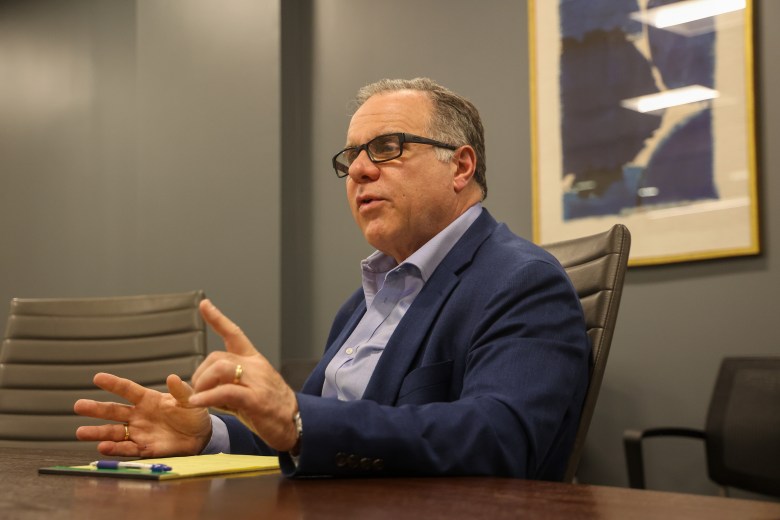 A man speaking. He is wearing a blue button-down shirt and a darker blue blazer.