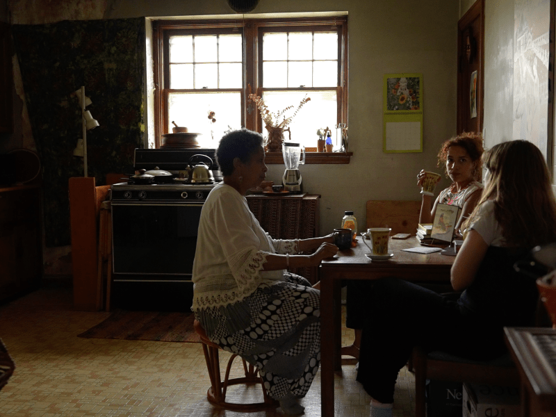 Three figures are seated at a table in converation.