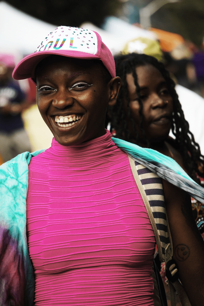 A person wearing a pink and white cap and bright pink top smiles for the camera